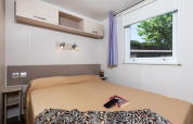 Dormitorio en la mobil home Cottage «Cesenatico» en Italia con cama doble, ventana y estanterías.