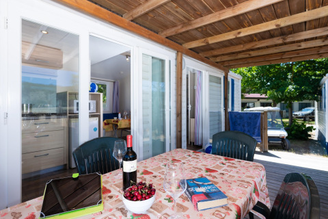 Terraza de la casa móvil Cottage 'Cesenatico' en Italia con mesa puesta, vino, cerezas y ambiente soleado.