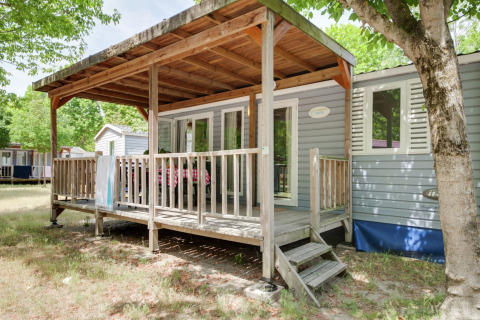 Mobilheim Cottage „Cesenatico“ in Italien, mit überdachter Holzveranda und umgeben von Bäumen.