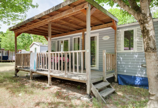 Casa móvil llamada Cottage «Cesenatico» en Italia, con porche de madera cubierto y rodeada de árboles.