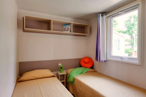 Helles Mobilheimzimmer im Cottage Cesenatico, Italien, mit zwei Einzelbetten, Regal und Fenster.