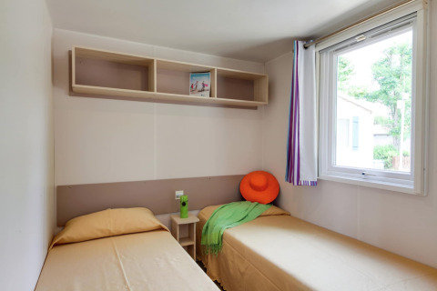 Helles Mobilheimzimmer im Cottage Cesenatico, Italien, mit zwei Einzelbetten, Regal und Fenster.