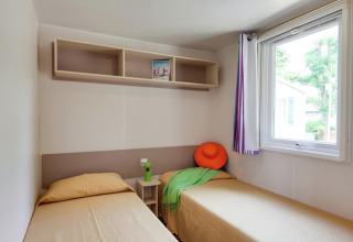 Helles Mobilheimzimmer im Cottage Cesenatico, Italien, mit zwei Einzelbetten, Regal und Fenster.