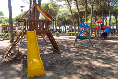 Speeltuin met glijbaan en schommels in schaduw bij stacaravan Luna Pineta, Italië.