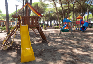 Speeltuin met glijbaan en schommels in schaduw bij stacaravan Luna Pineta, Italië.
