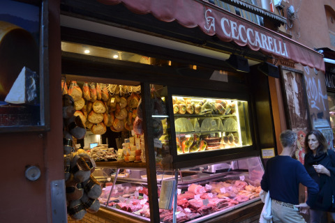 Buitenaanzicht van Italiaanse delicatessenzaak met hangende hammen, kaas en vlees bij Luna Pineta.