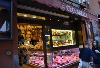 Buitenaanzicht van Italiaanse delicatessenzaak met hangende hammen, kaas en vlees bij Luna Pineta.