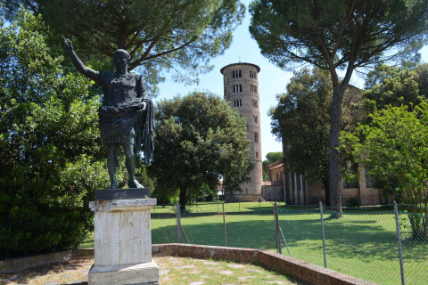 Standbeeld en historische toren bij Luna Pineta mobilhome, Italië, omgeven door groene bomen en zon.
