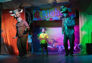 Presentación teatral en Cottage 'Cesenatico' en Italia, con dos adultos disfrazados y un niño en el escenario.