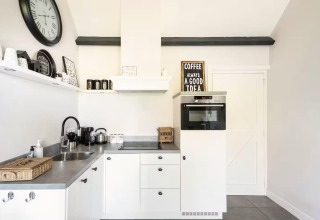 Bright, modern kitchen at Holiday home De Vlonder with coffee maker, wall clock, and sleek cabinets.