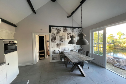 Lichte eetkamer in chalet Holiday home De Vlonder met houten tafel, fotowand en uitzicht op het water.