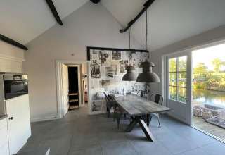 Lyst spisestue område i Holiday home De Vlonder chalet med træbord, store lamper og udsigt til vand.