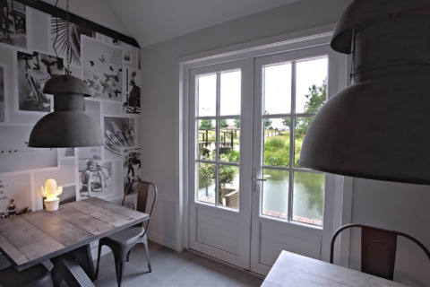 Moderne eethoek met grote ramen en uitzicht op water bij Holiday home De Vlonder, Nederland.
