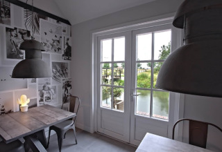 Moderne eethoek met grote ramen en uitzicht op water bij Holiday home De Vlonder, Nederland.