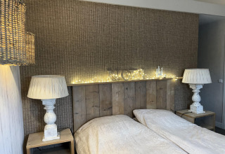 Bedroom at Holiday home De Vlonder, Netherlands, with twin beds, rustic wood, and cozy lamps and string lights.