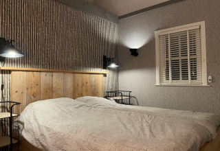 Slaapkamer in chalet 'Holiday home De Vlonder' in Nederland met tweepersoonsbed en wandlampen.