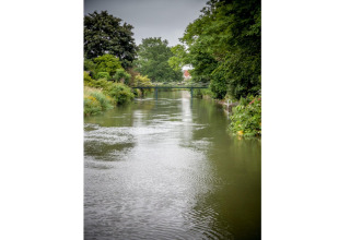 View of a calm river with lush trees and a small bridge at Holiday home De Vlonder in the Netherlands.