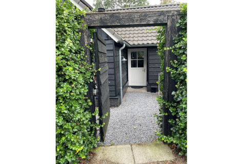 Indgang til Holiday home De Vlonder i Holland med sort port, grønne planter og grussti til døren.