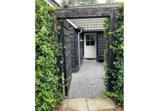 Indgang til Holiday home De Vlonder i Holland med sort port, grønne planter og grussti til døren.