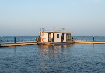 Casa galleggiante moderna chiamata Houseboat Agua Dolce ormeggiata in un porto tranquillo con acqua e cielo sullo sfondo.