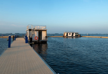 Photo de la péniche 'Agua Dolce' amarrée à un quai aux Pays-Bas, entourée d’eau calme et de ciel bleu.