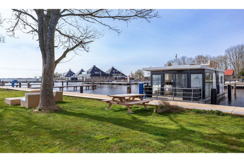 Hausboot «Agua Dolce» in den Niederlanden am Wasser, Picknicktisch und Sofas im Vordergrund.