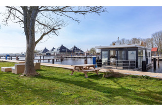 Hausboot «Agua Dolce» in den Niederlanden am Wasser, Picknicktisch und Sofas im Vordergrund.