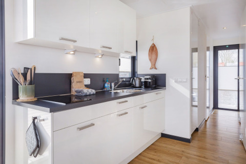 Moderne Küche auf dem Hausboot «Agua Dolce» in den Niederlanden mit weißen Schränken und Holzfußboden.