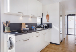 Cocina moderna en la casa flotante «Agua Dolce» en Holanda, con gabinetes blancos y encimera negra.
