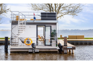 Casa flotante moderna 'Agua Dolce' atracada en los Países Bajos con terraza y vistas al lago.