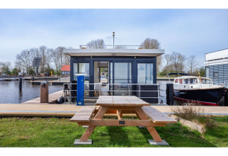 Hausboot „Agua Dolce“ in den Niederlanden mit Picknicktisch vorne, Wasser und Booten im Hintergrund.