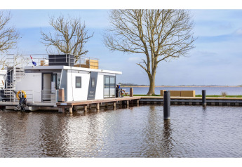 Péniche ‘Agua Dolce’ amarrée sur une rive paisible aux Pays-Bas, entourée d’arbres et d’eau.
