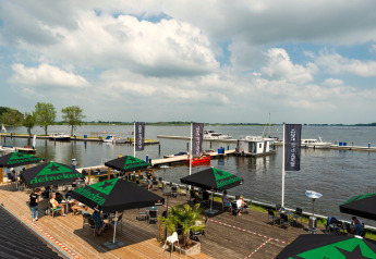 Blick auf das Wasser von Houseboat «Agua Dolce» in den Niederlanden, mit Terrasse, Sonnenschirmen und Booten.