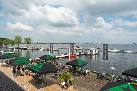 Blick auf das Wasser von Houseboat «Agua Dolce» in den Niederlanden, mit Terrasse, Sonnenschirmen und Booten.