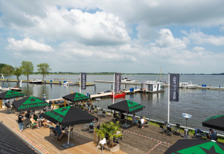 Blick auf das Wasser von Houseboat «Agua Dolce» in den Niederlanden, mit Terrasse, Sonnenschirmen und Booten.