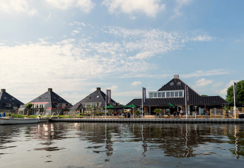 Blick auf Hausboote und moderne Gebäude am Wasser in den Niederlanden, mit Café-Terrasse am Ufer.