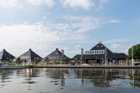 Blick auf Hausboote und moderne Gebäude am Wasser in den Niederlanden, mit Café-Terrasse am Ufer.