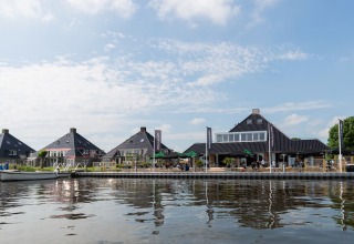Blick auf Hausboote und moderne Gebäude am Wasser in den Niederlanden, mit Café-Terrasse am Ufer.