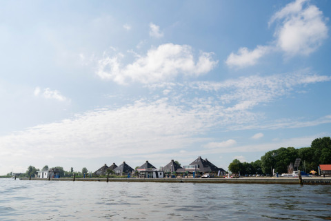 Blick auf das Hausboot „Agua Dolce“ in den Niederlanden, gelegen am ruhigen Wasser unter blauem Himmel.
