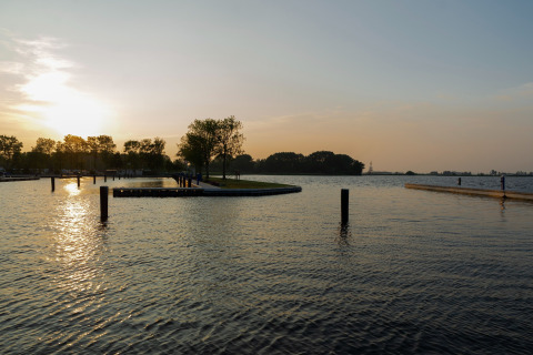 Sonnenuntergang am Wasser bei Houseboat 'Agua Dolce' in den Niederlanden, mit ruhigem See und Bäumen.
