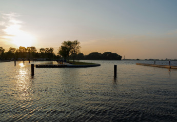 Tramonto sul lago visto da Houseboat 'Agua Dolce' nei Paesi Bassi, con acqua calma e alberi sullo sfondo.