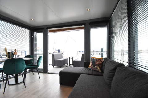 Modern living room on houseboat 'Boat' in the Netherlands with large windows, sofa, and dining area.
