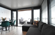 Modern living room on houseboat 'Boat' in the Netherlands with large windows, sofa, and dining area.