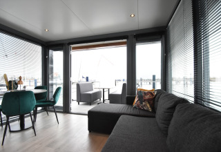 Modern living room on houseboat 'Boat' in the Netherlands with large windows, sofa, and dining area.