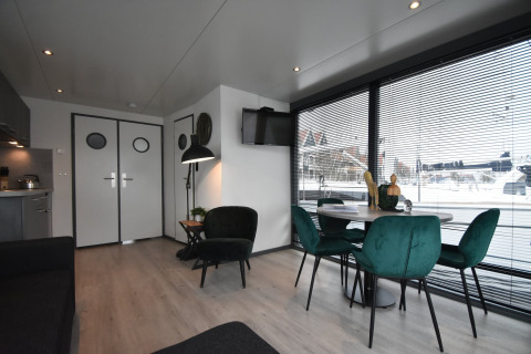 Modern houseboat 'Boat' interior in the Netherlands, with green chairs, dining table, and harbor views.