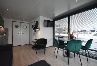 Modern houseboat 'Boat' interior in the Netherlands, with green chairs, dining table, and harbor views.