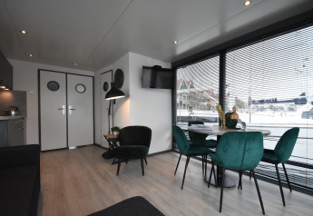 Modern houseboat 'Boat' interior in the Netherlands, with green chairs, dining table, and harbor views.