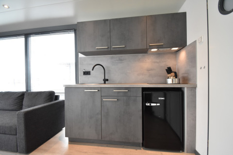 Modern kitchenette on houseboat 'Boat' in the Netherlands with gray cabinets, mini fridge and sofa.