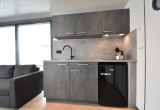 Modern kitchenette on houseboat 'Boat' in the Netherlands with gray cabinets, mini fridge and sofa.