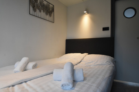 Modern houseboat bedroom in the Netherlands with double bed, fresh towels, and minimalistic decor.